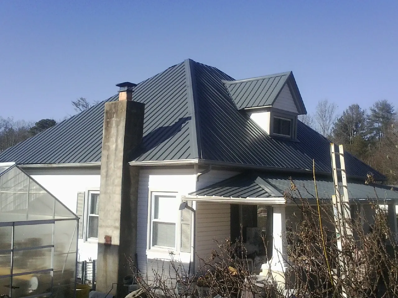 Dark blue standing seam metal roof on a white farmhouse with dormer — Slate & Tile Roof Repair by Roofing Brothers in London