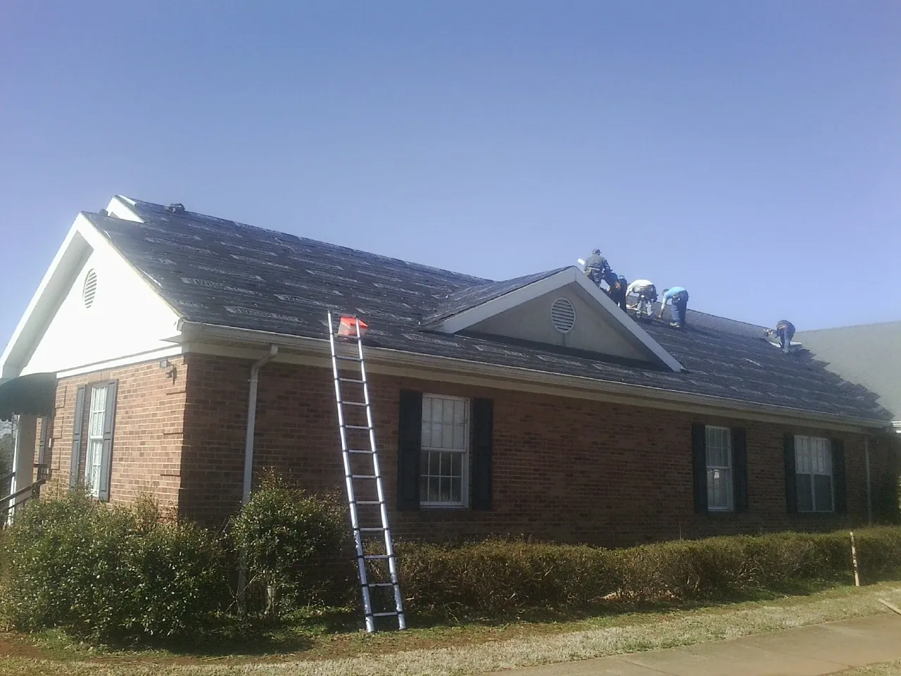 Crew tearing shingles off a brick ranch roof with a ladder set — Emergency Roof Repair work by our crew in London