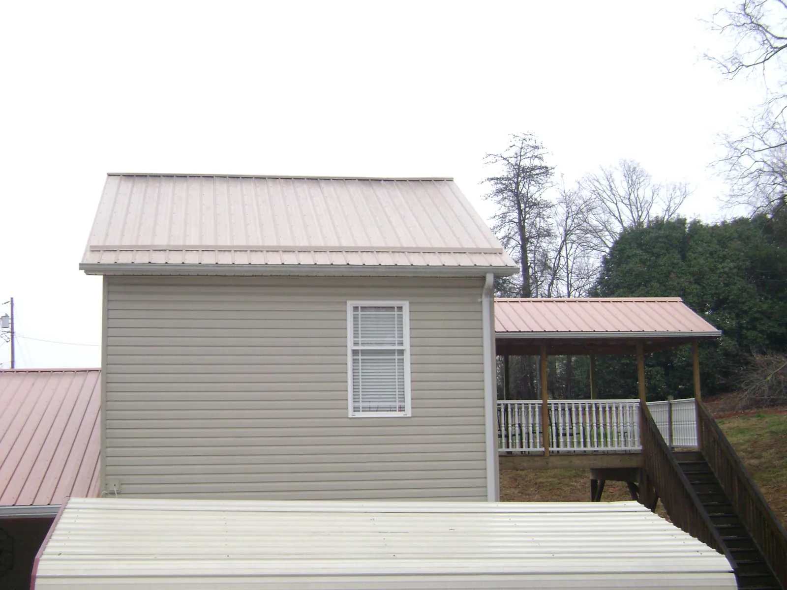 Tan metal roofs on a two story addition and attached porch, from a Roof Replacement job in London